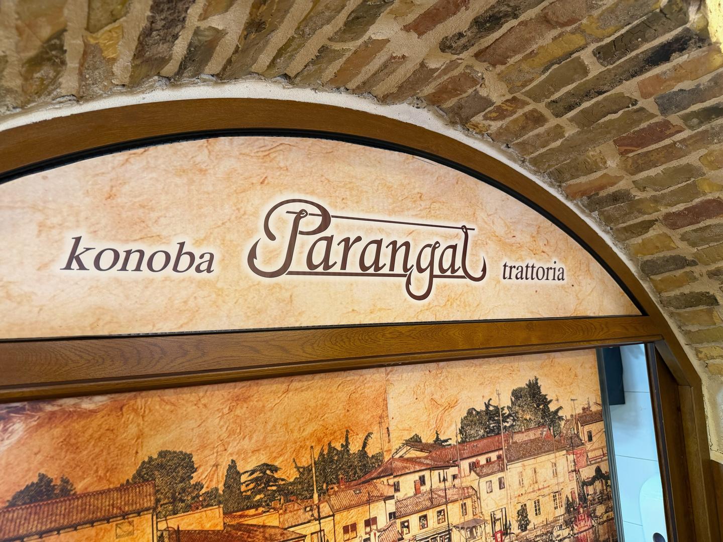 Kamenný oblouk s vytesaným jménem Parangal nad malovaným pohledem na Novigrad.