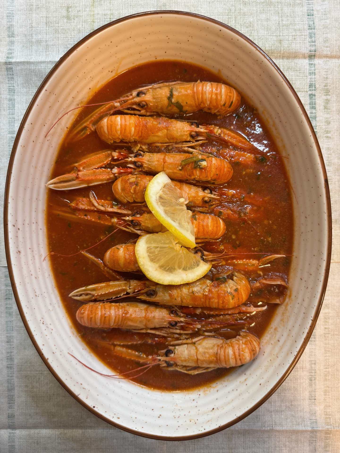 Scampi na buzaru v červené omáčce, v oválné misce, s plátky citronu.