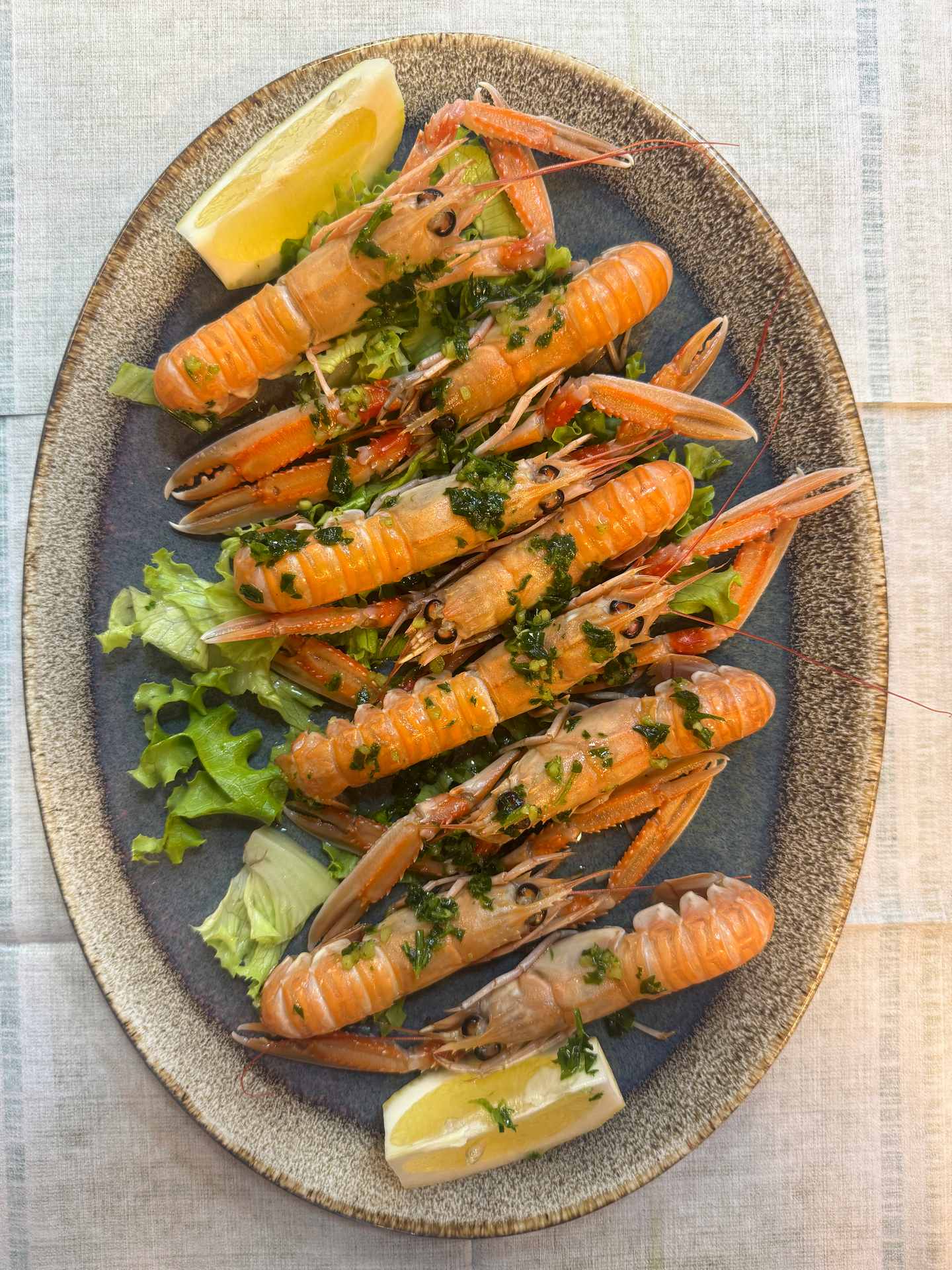 Grilované scampi na oválném talíři, s olivovým olejem a petrželí, plátky citronu.
